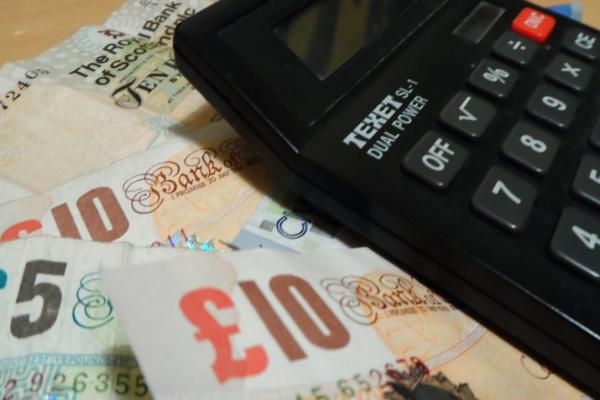 Black Texet calculator resting atop overlapping British pound notes, including £5 and £10 bills.